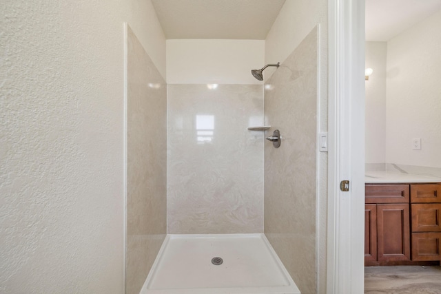 bathroom featuring vanity, a textured wall, and a tile shower