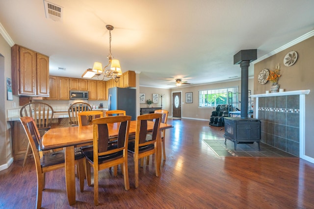 dining area with a wood stove, ornamental molding, dark wood-type flooring, and visible vents