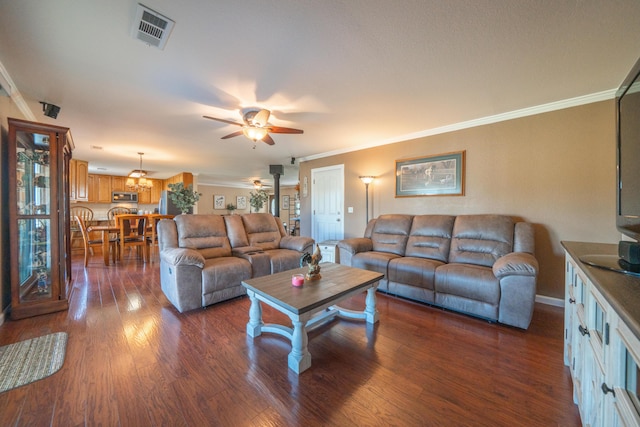 living room featuring crown molding, a ceiling fan, visible vents, and dark wood finished floors