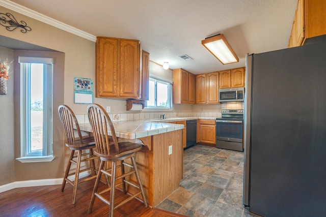 kitchen with a peninsula, stainless steel appliances, brown cabinets, tile countertops, and visible vents