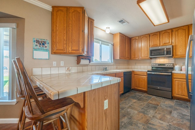 kitchen with a peninsula, a kitchen bar, tile countertops, visible vents, and appliances with stainless steel finishes