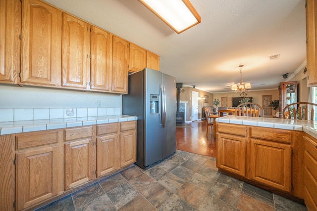 kitchen with stainless steel fridge, stone finish flooring, crown molding, visible vents, and tile countertops