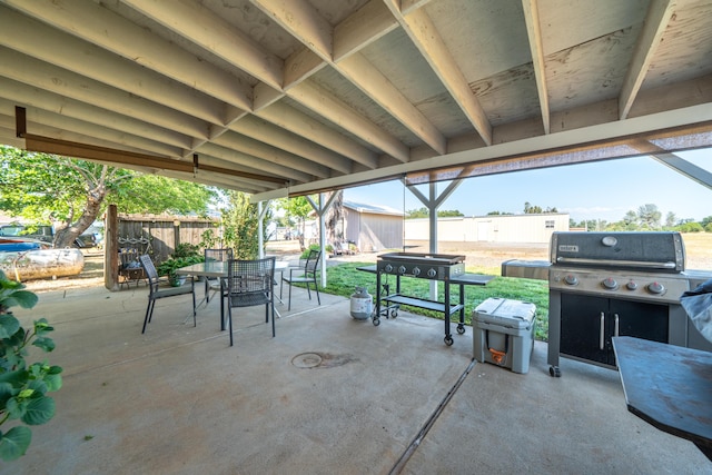 view of patio / terrace featuring an outbuilding, outdoor dining space, fence, a grill, and a storage shed