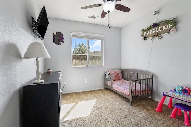bedroom with baseboards, visible vents, a nursery area, ceiling fan, and carpet