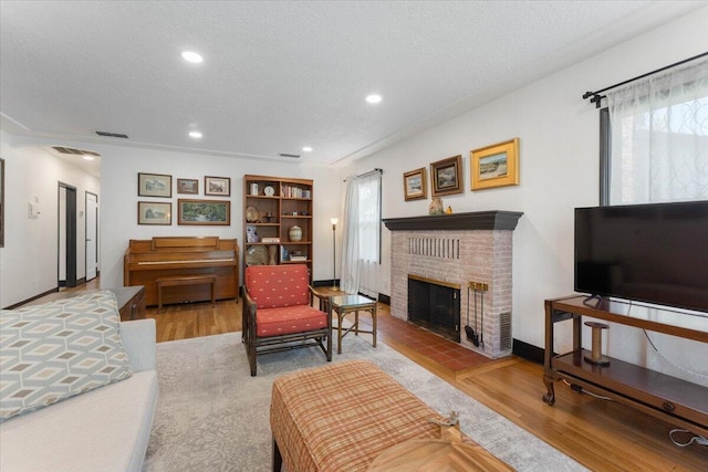 living room featuring plenty of natural light, a brick fireplace, a textured ceiling, and wood finished floors