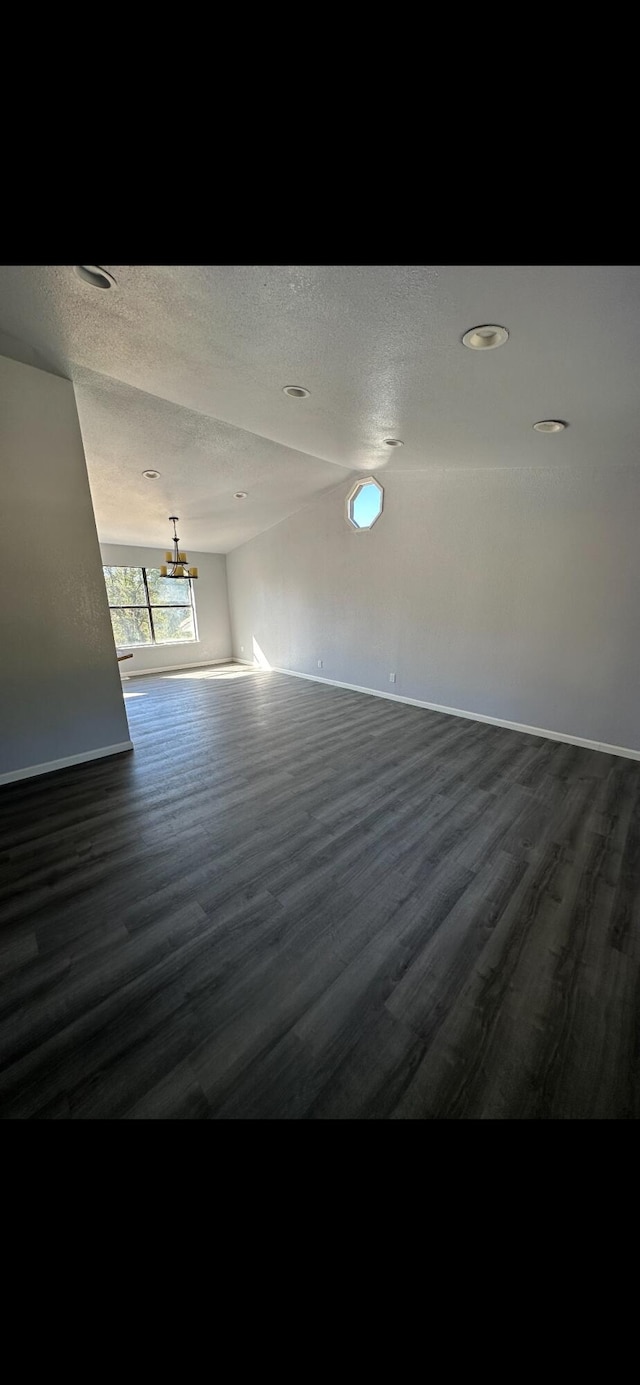 unfurnished room with baseboards, a textured ceiling, dark wood-style floors, and an inviting chandelier