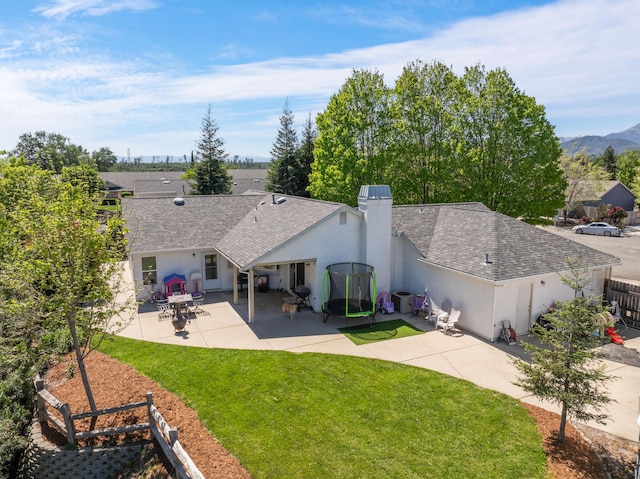 back of house featuring a lawn, a patio area, a shingled roof, and stucco siding