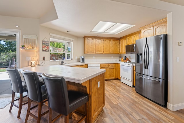 kitchen with tile counters, light wood-style floors, a breakfast bar, a peninsula, and white appliances