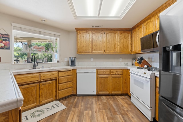 kitchen featuring a sink, visible vents, wood finished floors, white appliances, and brown cabinetry