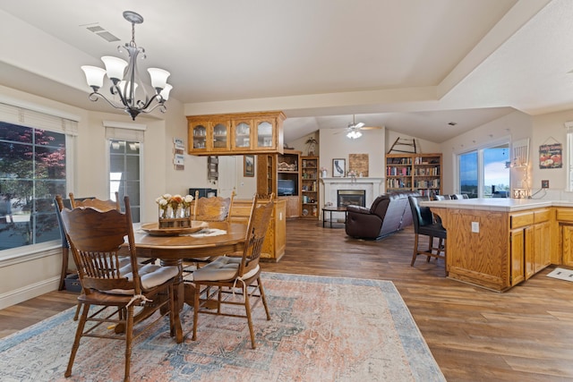 dining room with a glass covered fireplace, visible vents, wood finished floors, and ceiling fan with notable chandelier