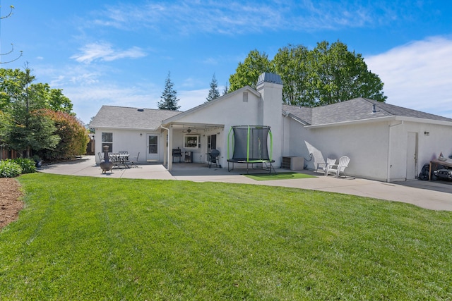 rear view of property featuring stucco siding, ceiling fan, a lawn, and a patio