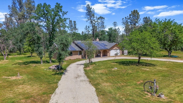view of front of home featuring a chimney, curved driveway, roof mounted solar panels, and a front yard