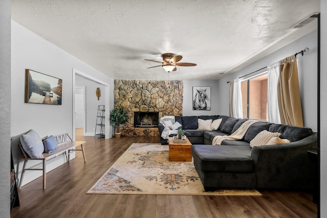 living area with ceiling fan, a stone fireplace, dark wood-style floors, visible vents, and a textured ceiling