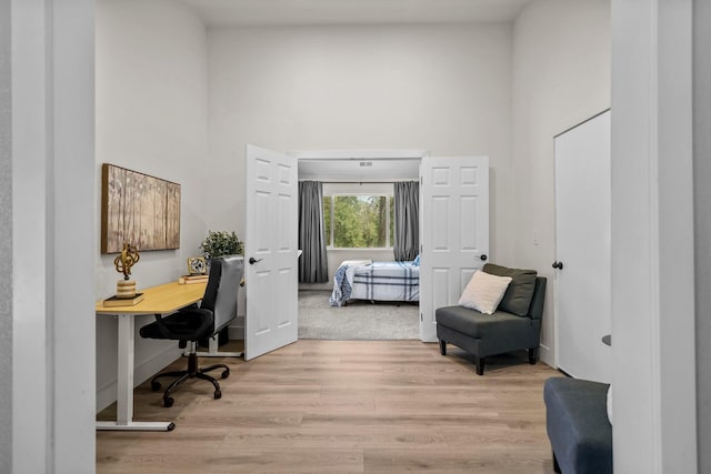 home office with a towering ceiling and light wood-style flooring