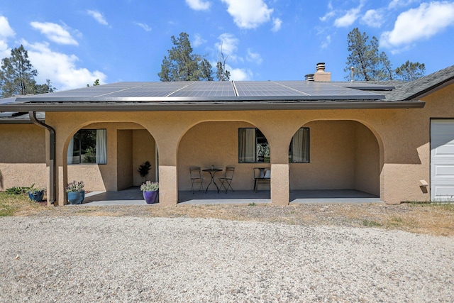 back of property with a chimney, solar panels, and stucco siding