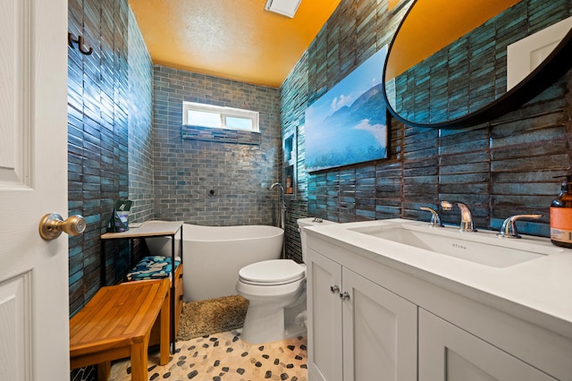 bathroom featuring tile walls, vanity, a freestanding bath, and toilet