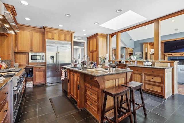 15320 Middletown Park Dr, Redding, CA 96001 - kitchen with built in appliances, a skylight, ventilation hood, an island with sink, and dark stone counters