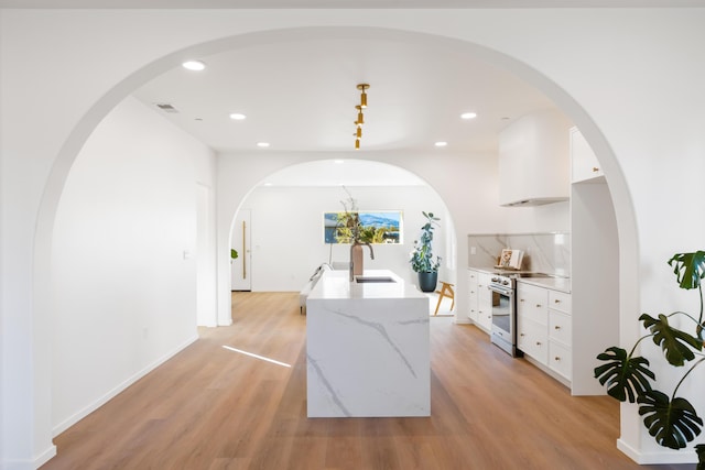kitchen featuring stainless steel stove, a sink, light wood finished floors, white cabinets, and recessed lighting