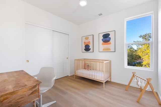 bedroom with light wood finished floors, a crib, visible vents, and a closet
