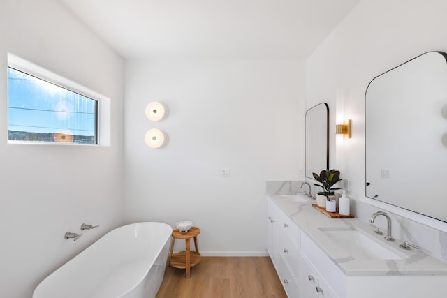 bathroom with a freestanding bath, double vanity, wood finished floors, and a sink