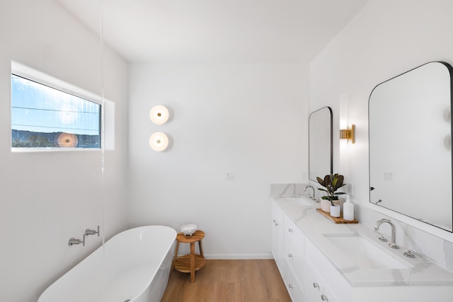 full bathroom with a freestanding bath, double vanity, wood finished floors, and a sink