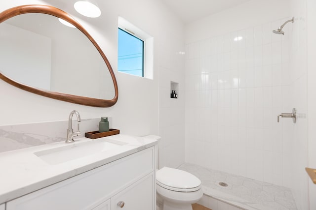 bathroom with a tile shower, toilet, and vanity