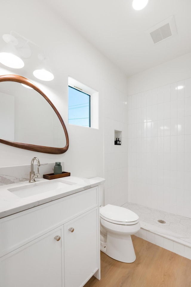 bathroom featuring toilet, tiled shower, visible vents, wood finished floors, and vanity