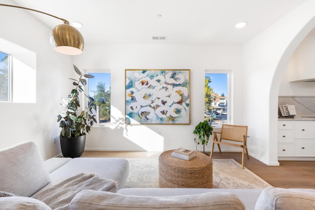 living area with arched walkways, plenty of natural light, visible vents, and wood finished floors