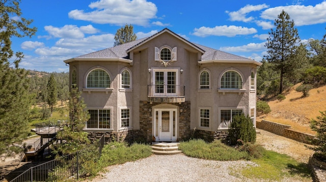 mediterranean / spanish house with a balcony, stone siding, stucco siding, and fence