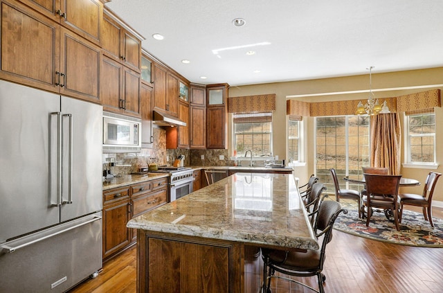 kitchen with a sink, dark wood-style flooring, light stone countertops, under cabinet range hood, and high quality appliances