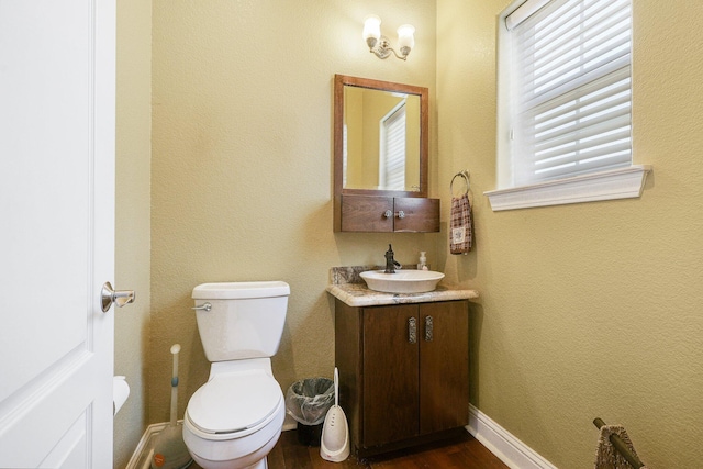half bath featuring baseboards, wood finished floors, vanity, and toilet