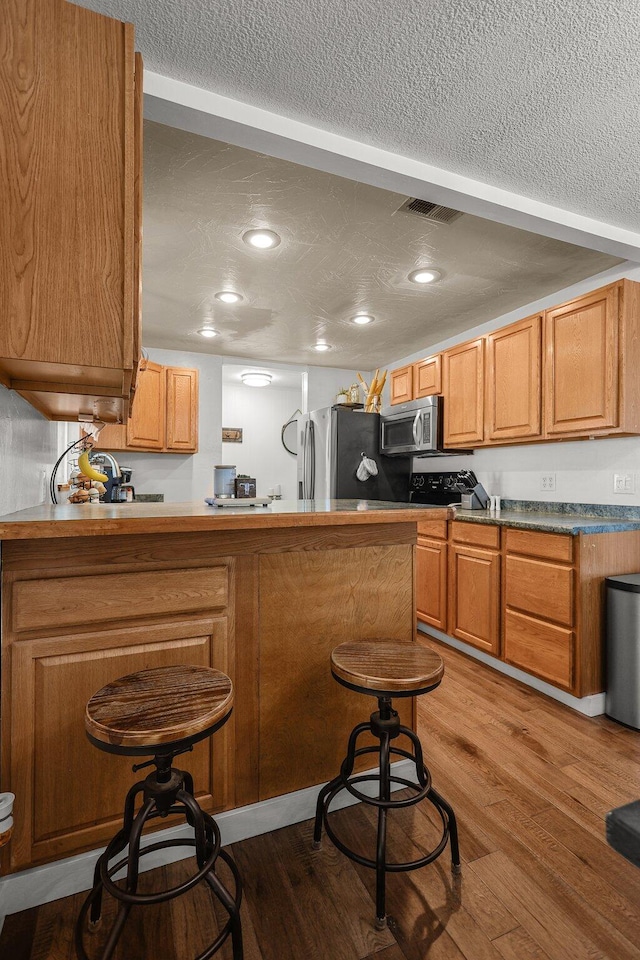 4647 County Road Ff, Orland, CA 95963 - kitchen with appliances with stainless steel finishes, a textured ceiling, a breakfast bar area, light wood-style flooring, and a peninsula