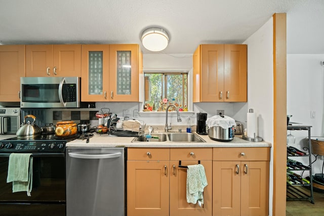 kitchen featuring a sink, decorative backsplash, glass insert cabinets, light countertops, and appliances with stainless steel finishes