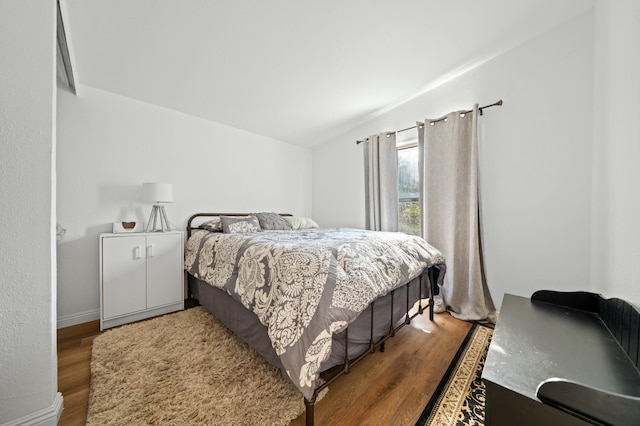bedroom with vaulted ceiling, wood finished floors, and baseboards