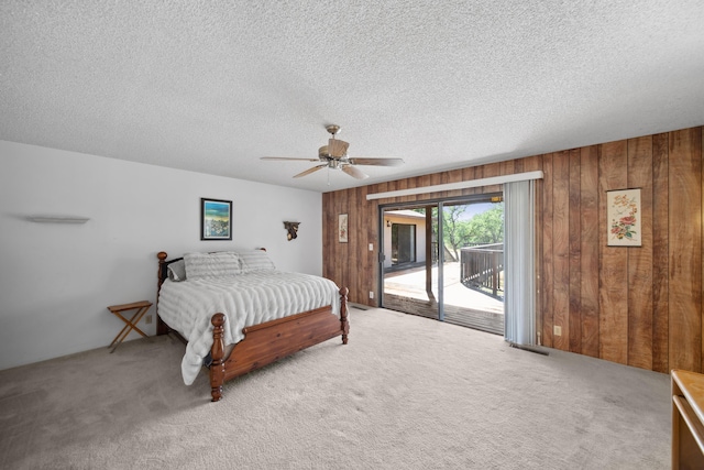 carpeted bedroom with visible vents, access to exterior, wooden walls, a textured ceiling, and a ceiling fan