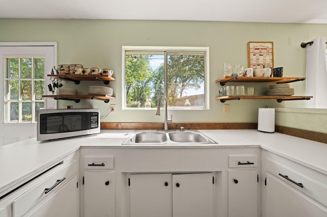 kitchen with stainless steel microwave, open shelves, a sink, and white cabinets