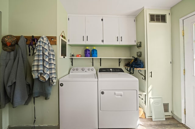 washroom featuring washing machine and dryer, cabinet space, visible vents, and light wood-style flooring