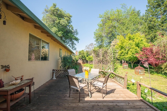 wooden deck featuring a lawn, fence, and outdoor dining space