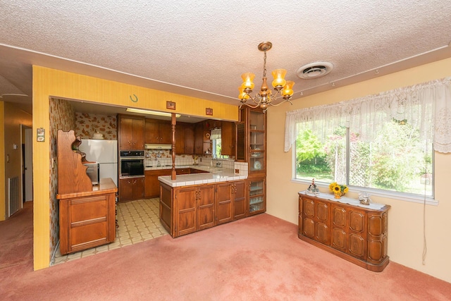 kitchen featuring oven, visible vents, freestanding refrigerator, a chandelier, and brown cabinetry