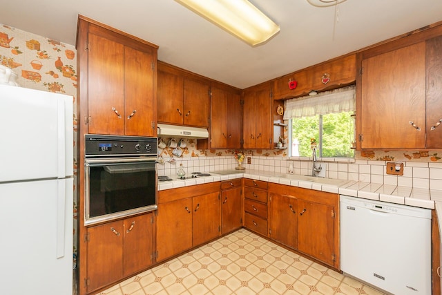 kitchen featuring a sink, decorative backsplash, white appliances, light floors, and under cabinet range hood