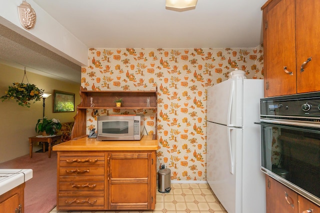 kitchen with brown cabinets, freestanding refrigerator, and black oven