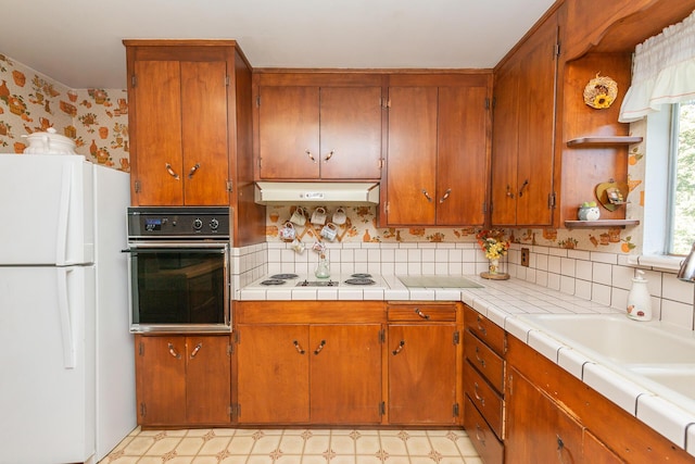 kitchen with brown cabinetry, decorative backsplash, white appliances, light floors, and under cabinet range hood
