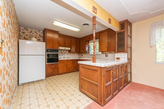 kitchen with plenty of natural light, brown cabinets, black oven, visible vents, and freestanding refrigerator