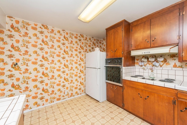 kitchen with brown cabinets, wallpapered walls, under cabinet range hood, light floors, and white appliances