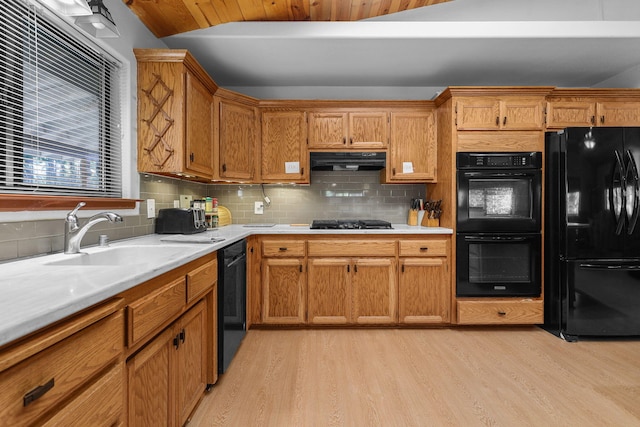 kitchen with a sink, light wood-style floors, light countertops, under cabinet range hood, and black appliances