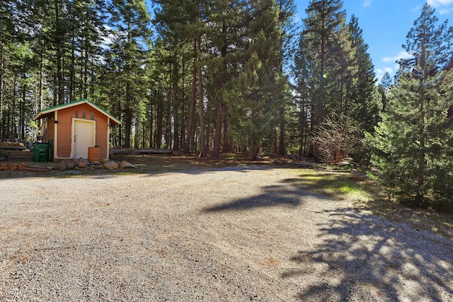 view of yard featuring an outdoor structure, a storage unit, and a wooded view
