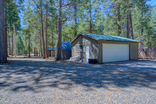 detached garage featuring fence and a wooded view