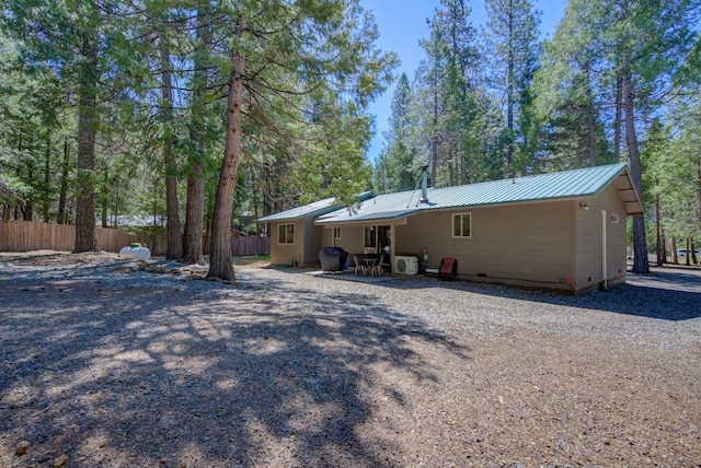 back of property featuring fence, crawl space, gravel driveway, and metal roof