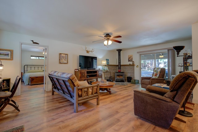 living area with ceiling fan, a healthy amount of sunlight, a wood stove, and light wood finished floors