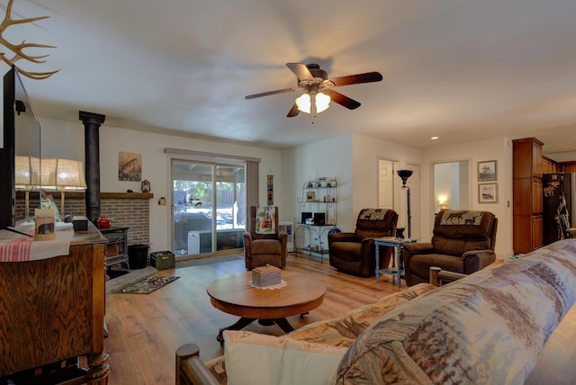 living area with a ceiling fan, a wood stove, and light wood finished floors